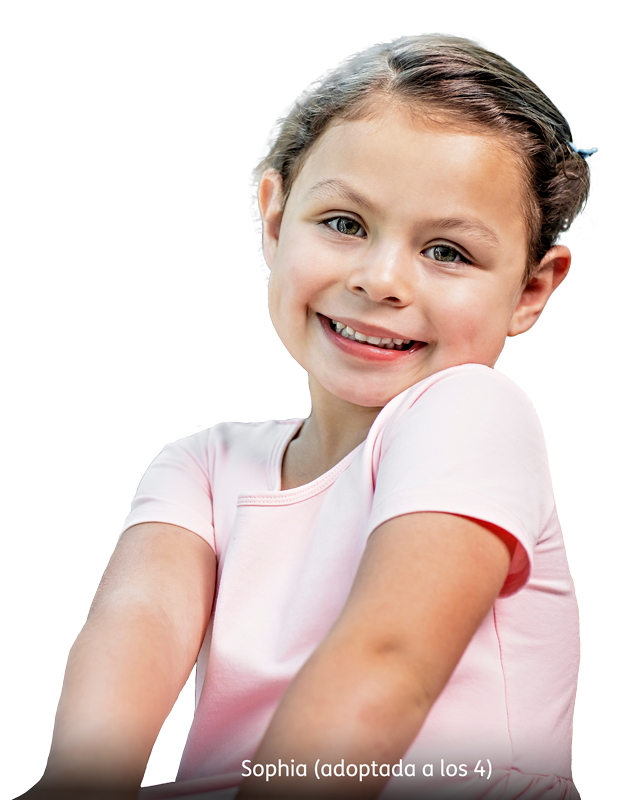 A young girl with light skin and blue eyes smiles while wearing a light pink shirt. Her brown hair is pulled back. The text at the bottom reads “Sophia (adoptada a los 4).”.