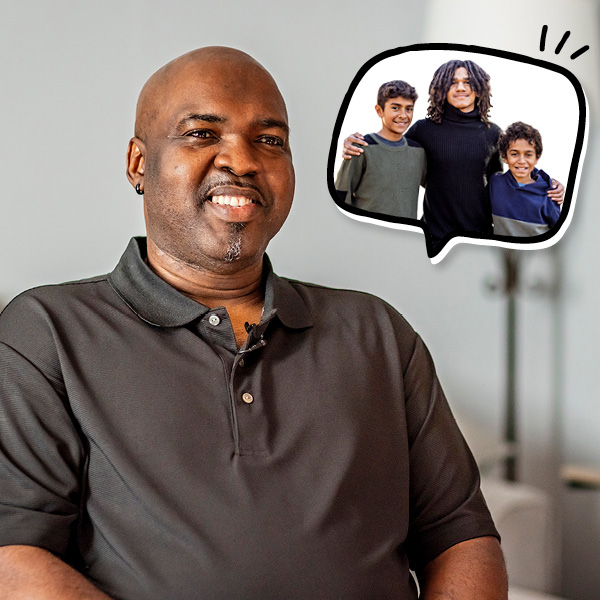 A smiling man in a black polo shirt sits indoors. A thought bubble above him shows a person with long hair standing with two children, all smiling.