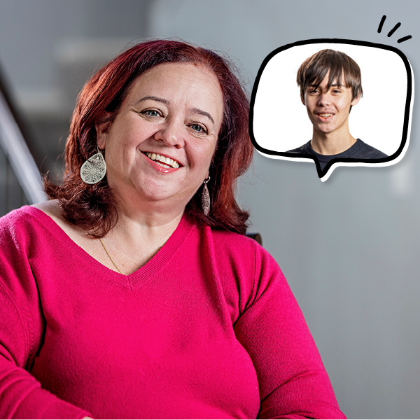 A woman with red hair and a pink sweater smiles while sitting indoors. A thought bubble with a young man’s portrait is shown near her head, indicating she is thinking about him.