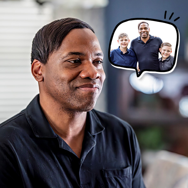 A man in a black shirt smiles softly, while a thought bubble shows him happily posing with two smiling boys, all dressed in dark shirts.