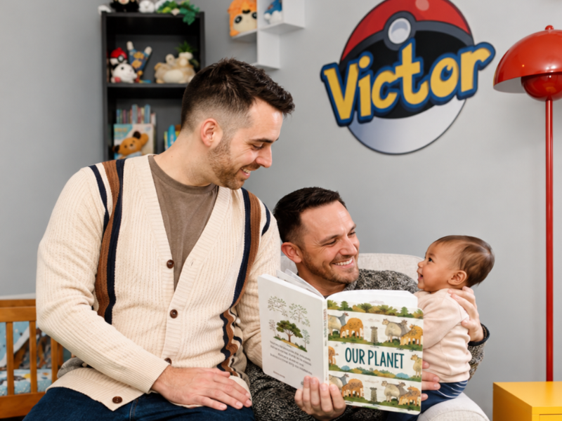 Two adults sit in a nursery reading Our Planet to a baby. Behind them, a bookshelf holds toys and books, and a large Poké Ball graphic with the name Victor is on the wall.